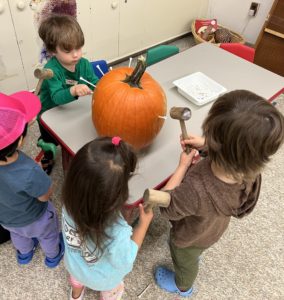 A group of students stands around a table hammering golf tees into a pumpkin